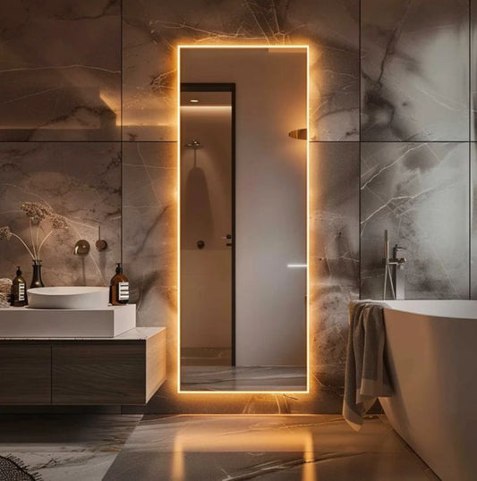Modern bathroom with a large illuminated mirror and marble walls.