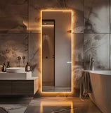 Modern bathroom with a large illuminated mirror and marble walls.