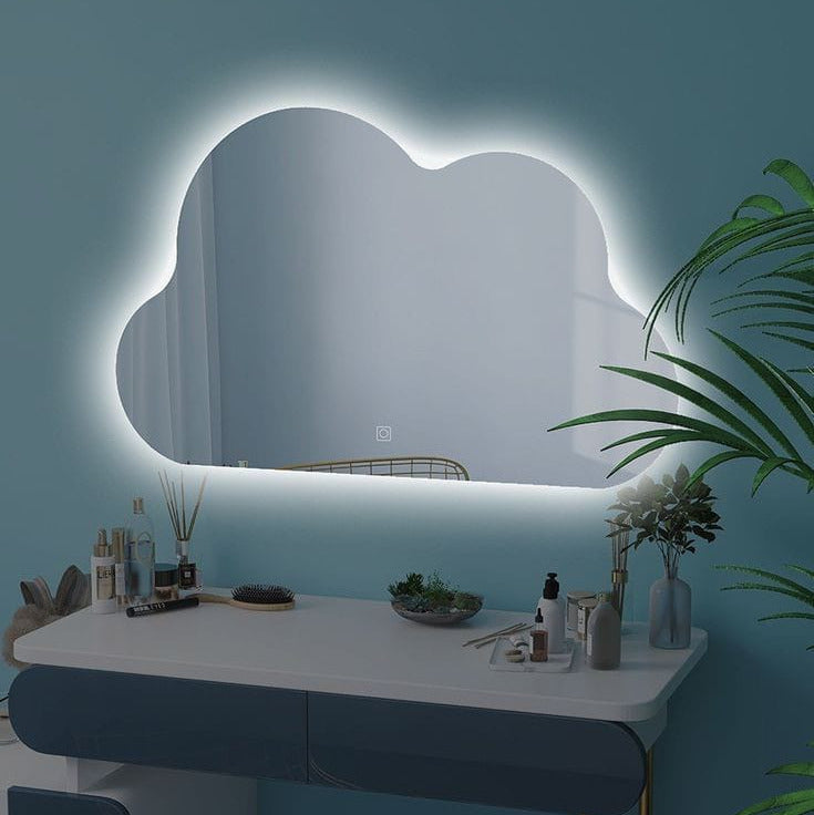 Modern vanity table with cloud-shaped mirror and decorative items against a blue wall.